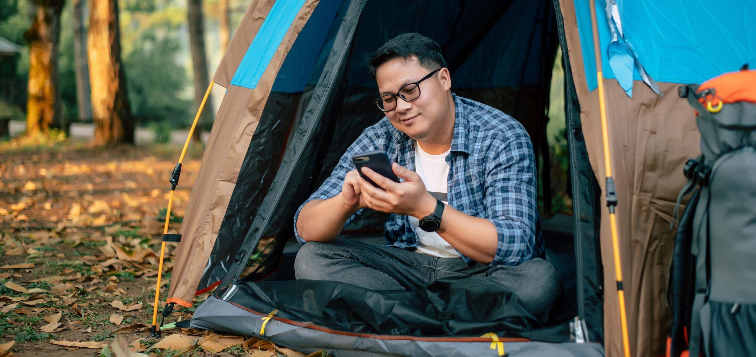 Portrait of Asian traveler man glasses using smartphone in tent