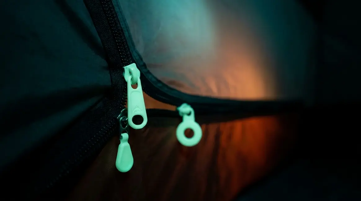Glow tent zipper pulls glowing green on a dark tent zipper at night